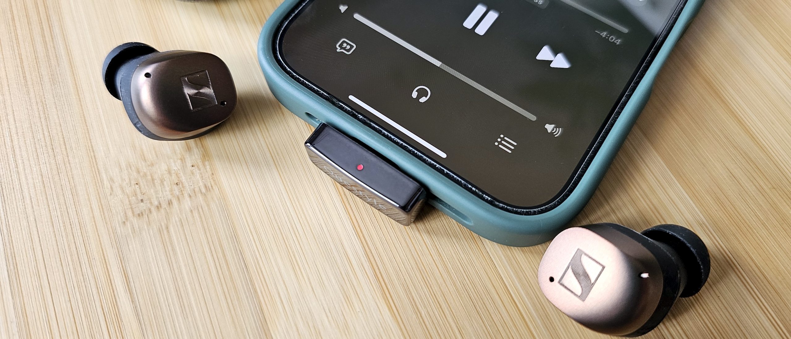 The Questyle QCC Dongle Pro with a smartphone to denote size, on a light wooden table